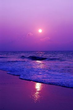 the sun is setting over the ocean with waves coming in to shore and purple sky