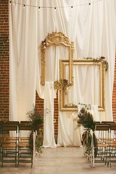 an outdoor ceremony with white drapes and gold framed photo frames on the wall, decorated with flowers and greenery