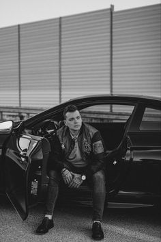 a man sitting in the open door of a car with his hand on his hip