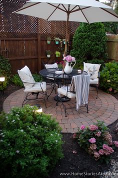 a patio with chairs and an umbrella in the middle of it, surrounded by flowers