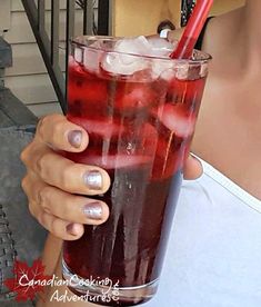 a woman holding up a tall glass filled with ice and red liquid on top of it