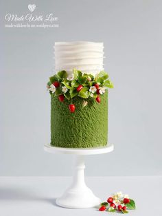 a green cake with strawberries and flowers on top is sitting on a white pedestal