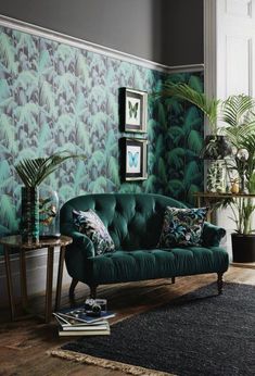 a green couch sitting in front of a wall covered in plants and palm leafy wallpaper