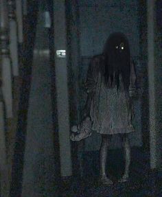 a woman with long hair walking down a dark hallway