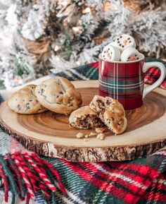 cookies and milk are on a wooden tray next to a plaid blanket with a cup of hot chocolate