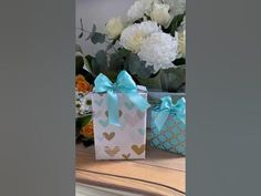 two small gift bags with blue bows are sitting on a table in front of flowers