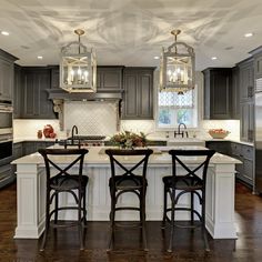 a kitchen with gray cabinets and white counter tops, two bar stools at the center