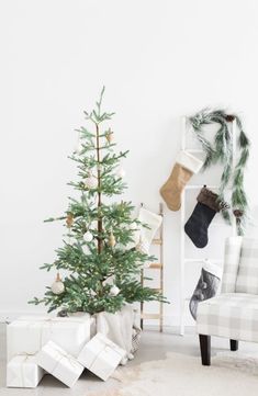 a small christmas tree sitting in front of a white couch with presents under it and stockings on the back