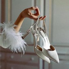 a woman's hand holding a pair of white high heels with feathers on them