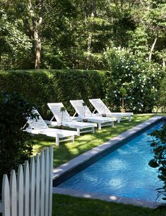 white lawn chairs line the edge of a pool in a backyard with lush green grass