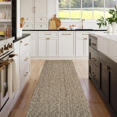 a kitchen with white cabinets and wood flooring next to an oven, counter top and sink