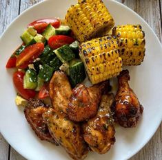 grilled chicken, corn on the cob and veggies are served on a white plate