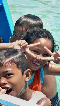 three children in a boat making the peace sign with their hands