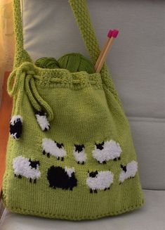 a green bag with black and white sheep painted on it sitting on a chair next to a knitting needle