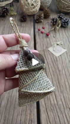 a hand holding a small christmas tree ornament on a wooden table with pine cones and twine