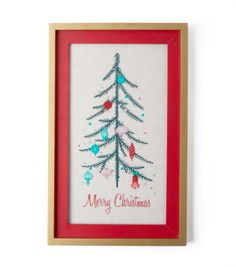 a cross stitch christmas tree in a red frame on a white wall with the words merry christmas