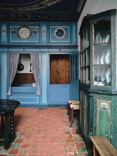 an old fashioned kitchen with blue walls and red brick flooring is seen in this image