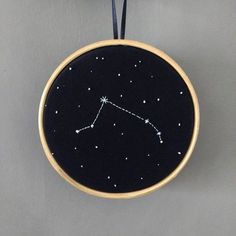 an embroidery hoop with a zodiac sign on it hanging from a hook in front of a wall