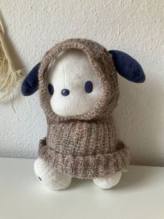 a small stuffed animal wearing a sweater on top of a white table next to a wall