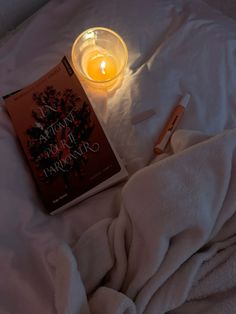 a candle and book on a bed with white sheets