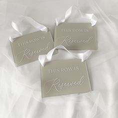 three signs that say this row is reserved on a white sheeted bed with satin ribbons