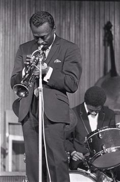 a man in a suit and tie plays the trumpet while another man stands behind him