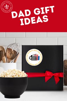 a black bowl filled with popcorn sitting on top of a counter next to a red and white sign that says dad gift ideas