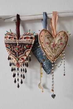 two heart shaped ornaments hanging from a clothes line with beads and tassels on them