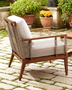 a wooden chair sitting on top of a stone floor next to potted plants and flowers