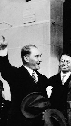 black and white photograph of two men standing next to each other with their arms in the air