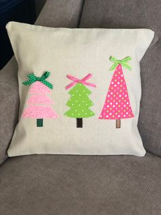 three christmas trees on a white pillow sitting on a gray couch with polka dot trim