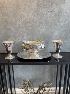 a table with three silver dishes on it and two vases sitting next to each other