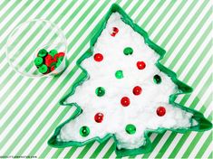 a decorated christmas tree shaped cookie next to a glass ornament on a green and white striped tablecloth