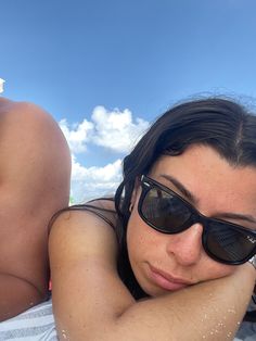 a woman laying on top of a beach next to a man in the water wearing sunglasses