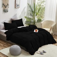 a bed with black sheets and pillows in a white room next to a plant on the floor