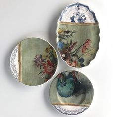 three plates with flowers painted on them sitting next to each other in front of a white wall