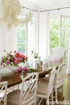 a dining room table with white chairs and pink flowers