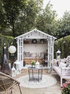 an outdoor living area with white furniture and lights on the ceiling, surrounded by greenery