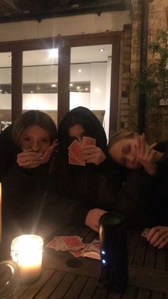 three women sitting at a table with cards in front of them and candles on the table