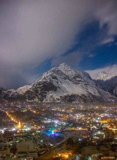 the city lights are lit up at night in front of snow - capped mountain peaks