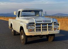 an old pickup truck is parked on the side of the road in front of some dry grass