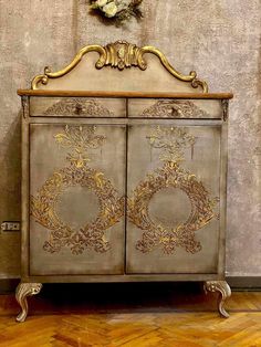 an ornate cabinet with gold paint on the doors and handles, in front of a wall