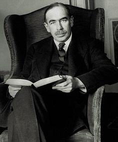 a man sitting in a chair holding a book and looking at the camera while reading it