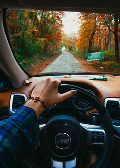 a person driving a car on a country road in the fall with trees and leaves