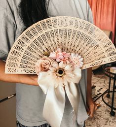 a woman holding a fan with flowers on it's side and a ribbon around the top