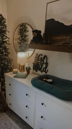 there is a teddy bear sitting on the dresser next to the mirror and christmas tree