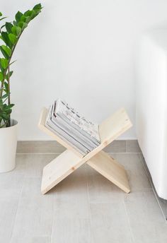 a wooden bench with magazines on it next to a potted plant and white walls