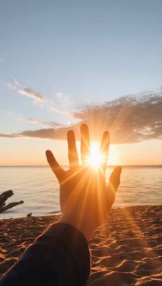 someone is holding their hand up in the air on a beach with the sun setting behind them