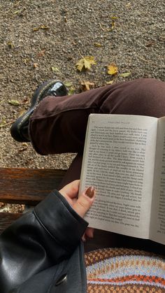 a person sitting on a bench reading a book with their legs crossed and one hand holding an open book