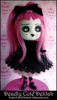 a doll with pink hair and black dress on top of a table in front of a wall